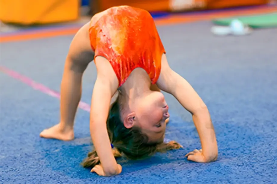 Young gymnast performing a backbend on mat.