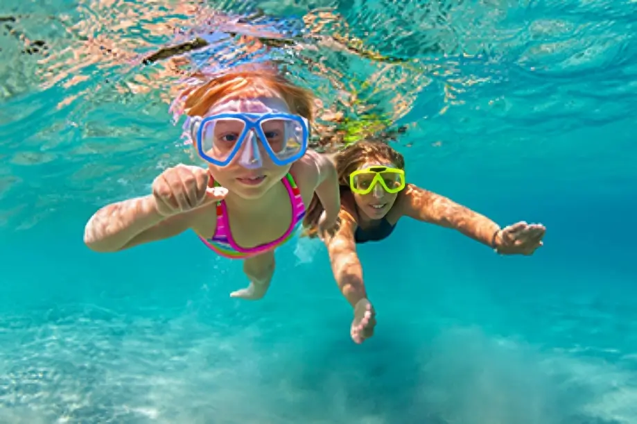 Two kids snorkeling underwater in clear ocean.